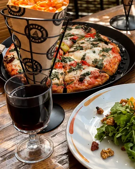 Roman style pizza with tomato, mozzarella and basil on a black pan beside a glass of red wine